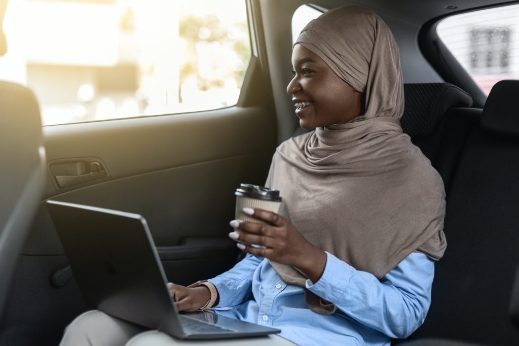 Black muslim businesswoman riding to office with laptop and coffee on backseat